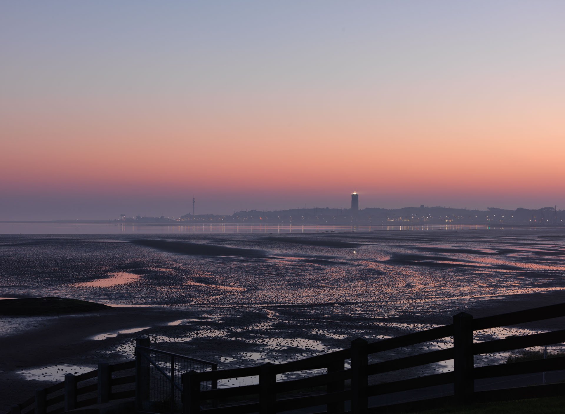 Distant lighthouse above tidal flats at dusk