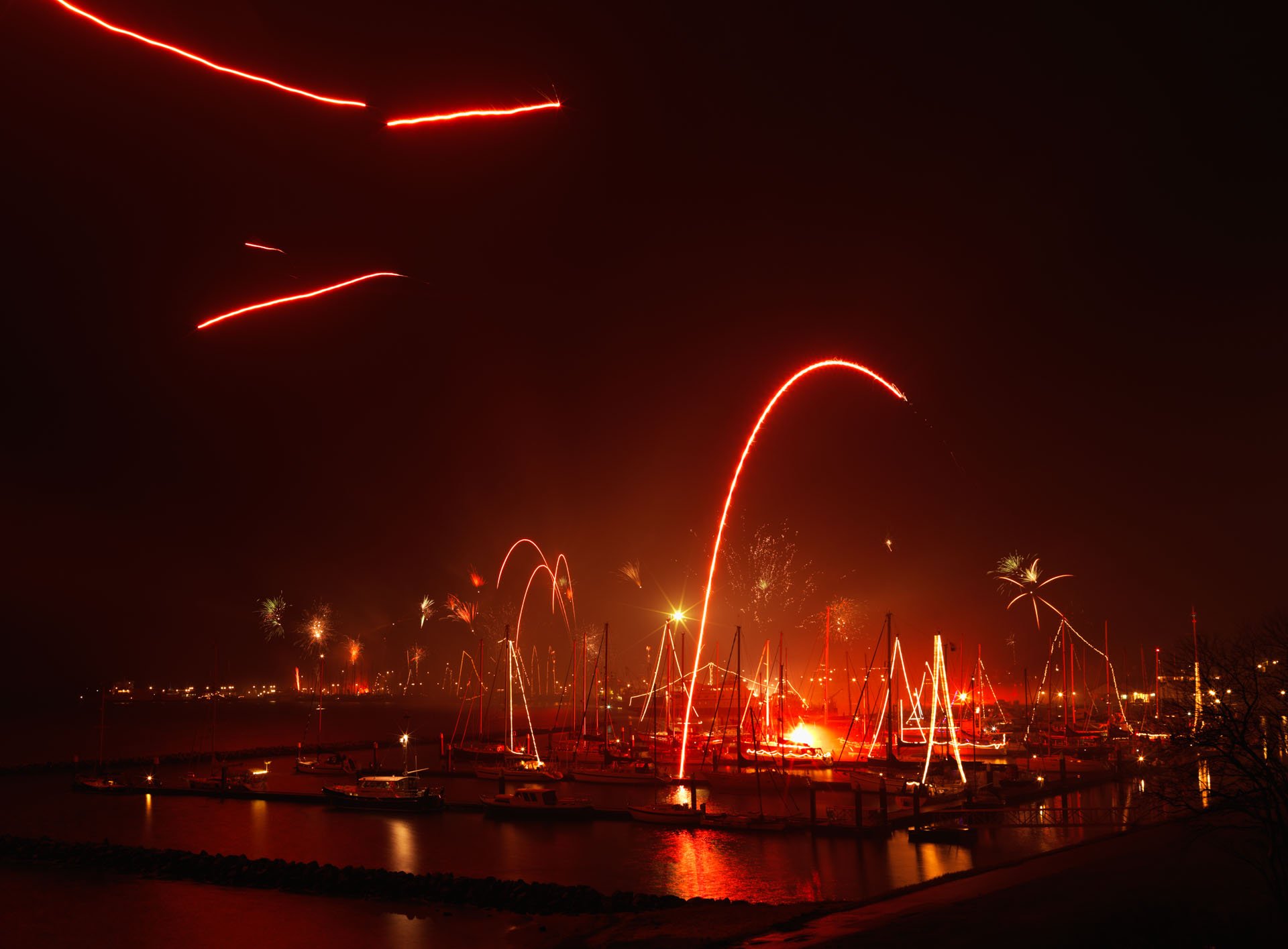 Red firework trails above a harbour at night