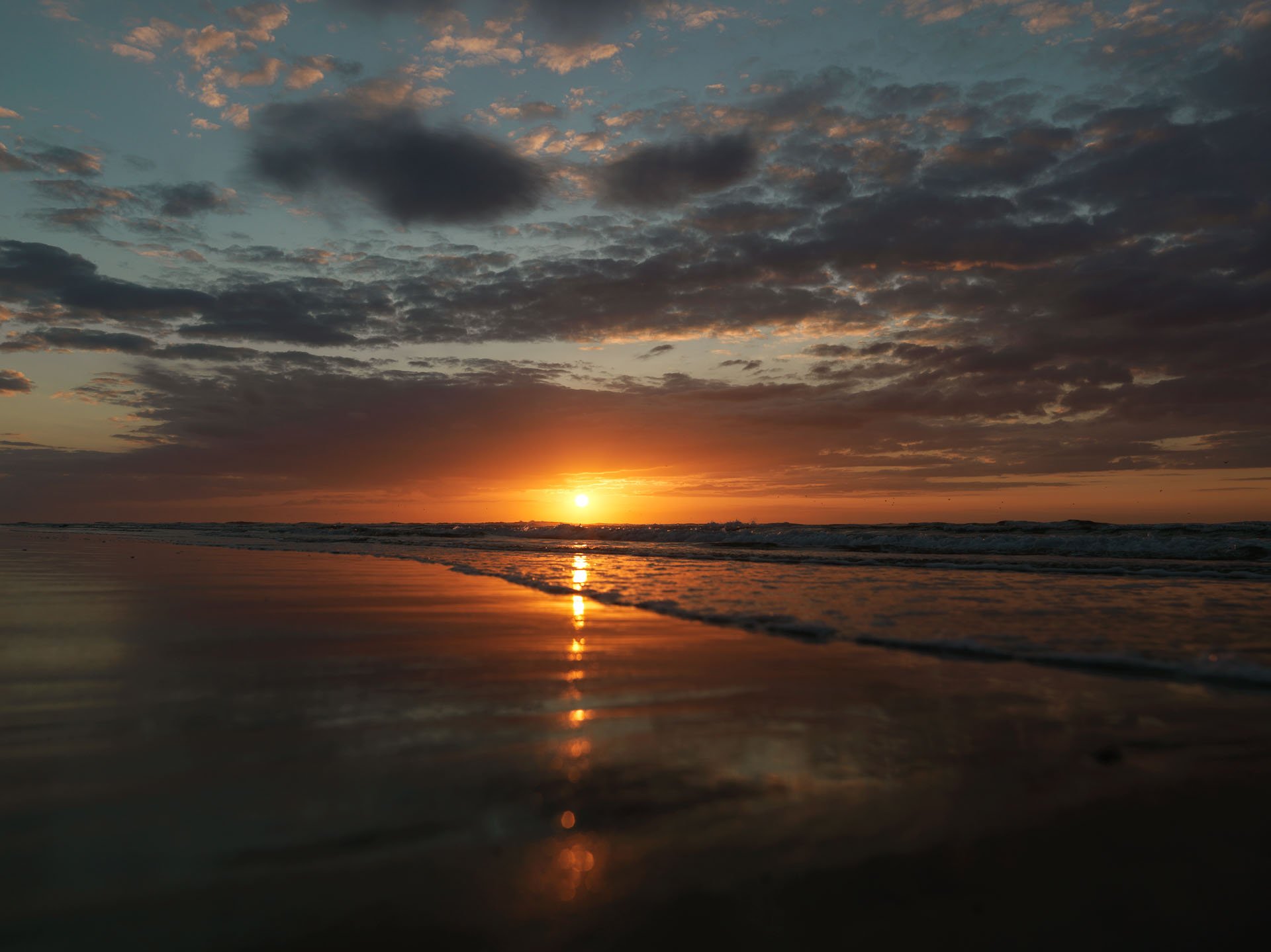 Orange sunset reflected on wet sand beneath dark clouds