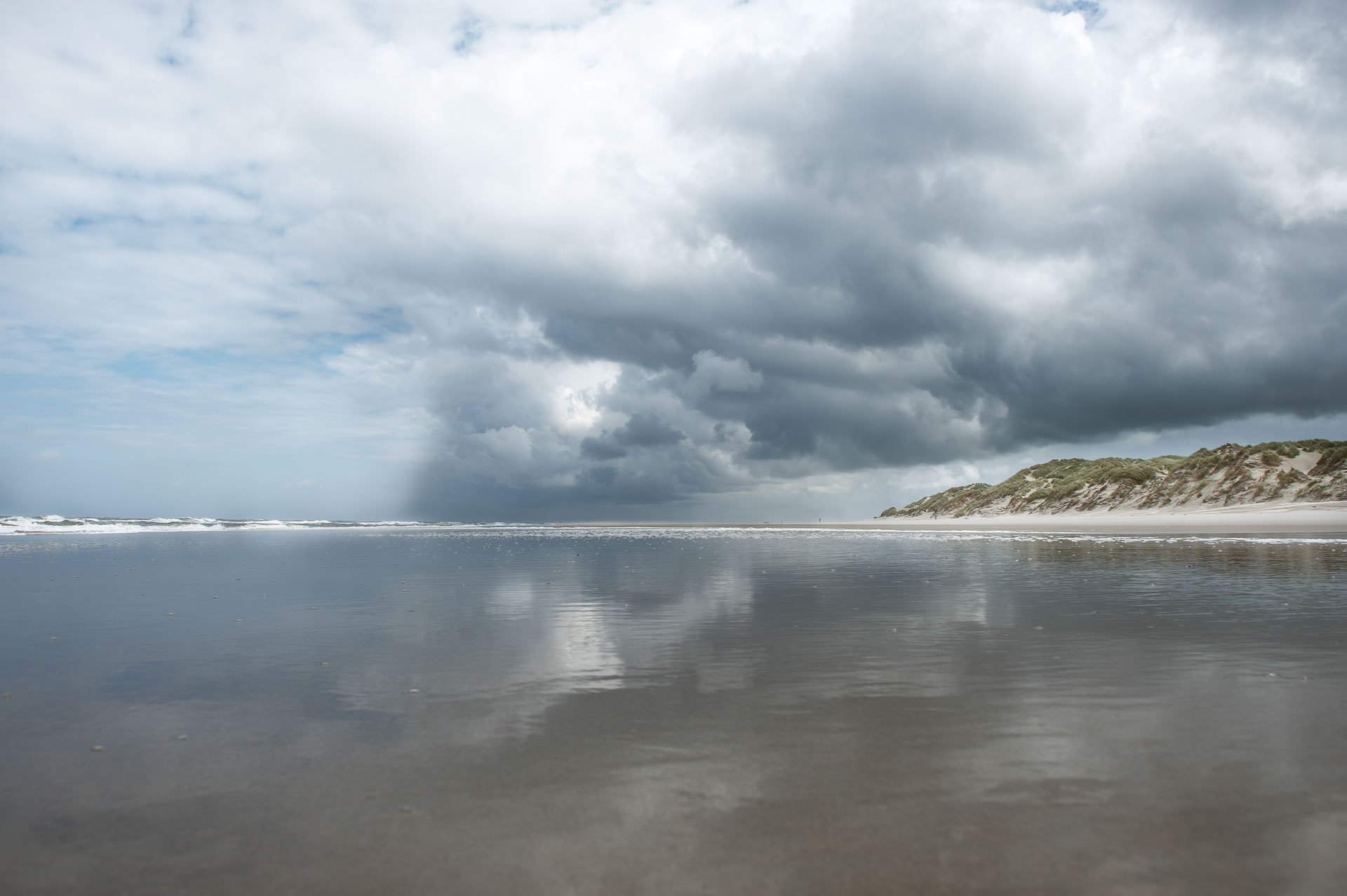 Clouds reflected on a wet beach beside dunes