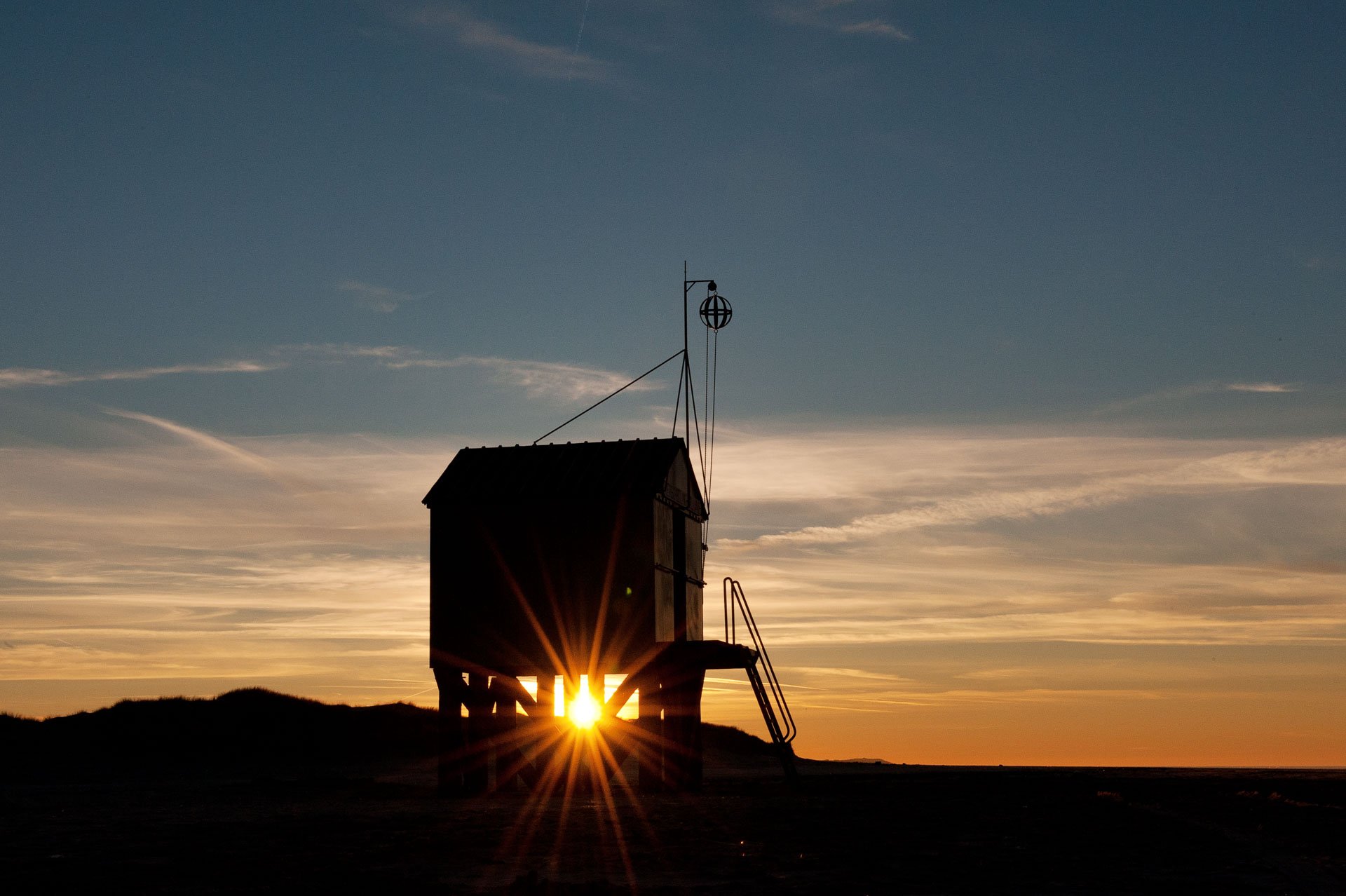 Beach hut on stilts silhouetted against the setting sun