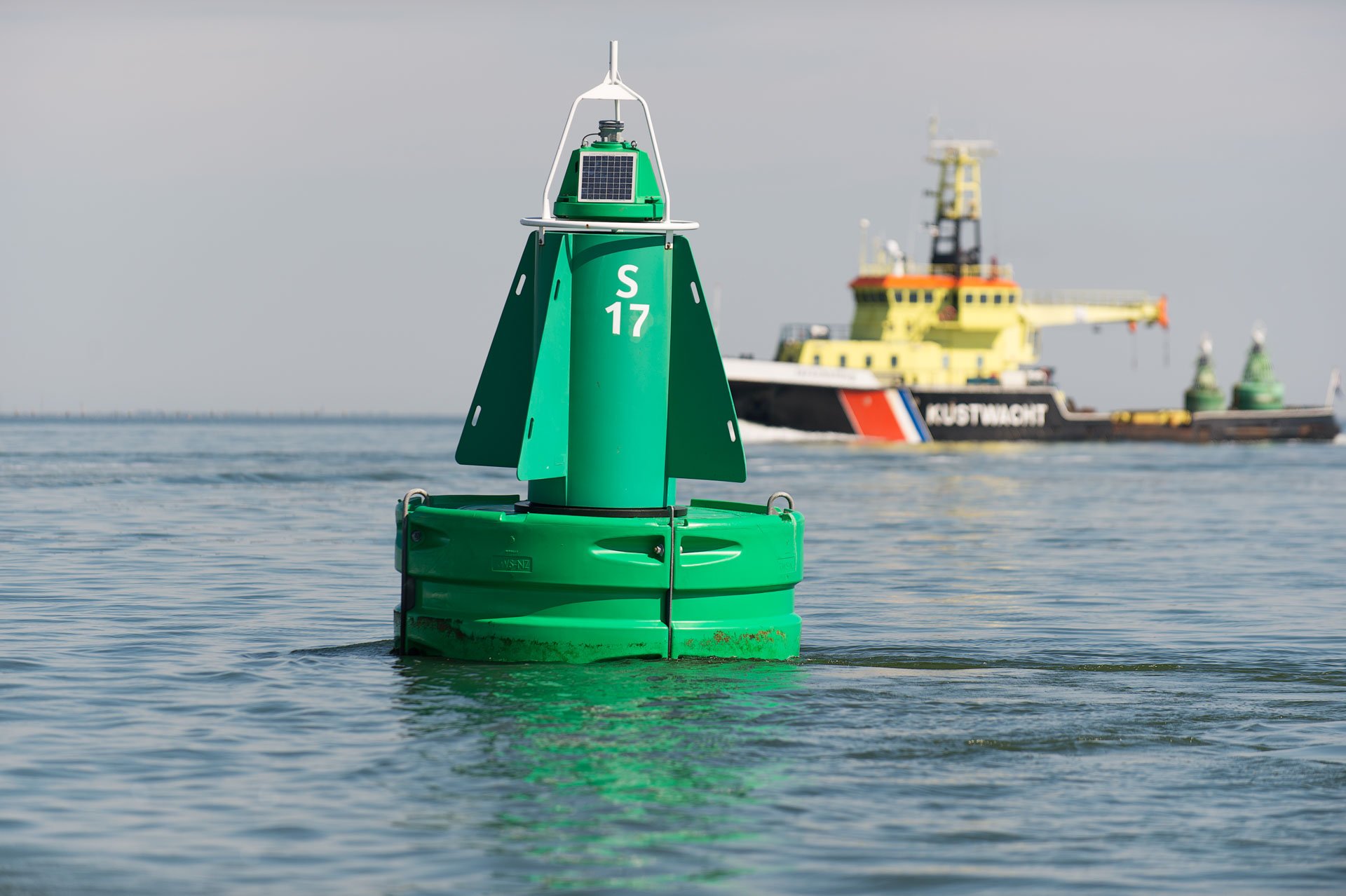 Green navigation buoy with a ship in the background