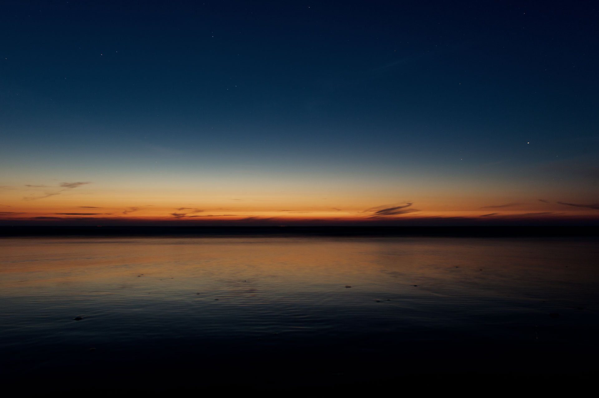 Orange horizon above dark water at dusk